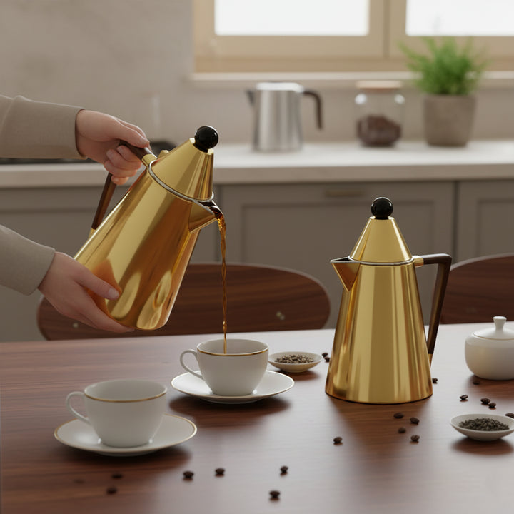 Person pouring coffee from a gold kettle into a white cup on a wooden table.