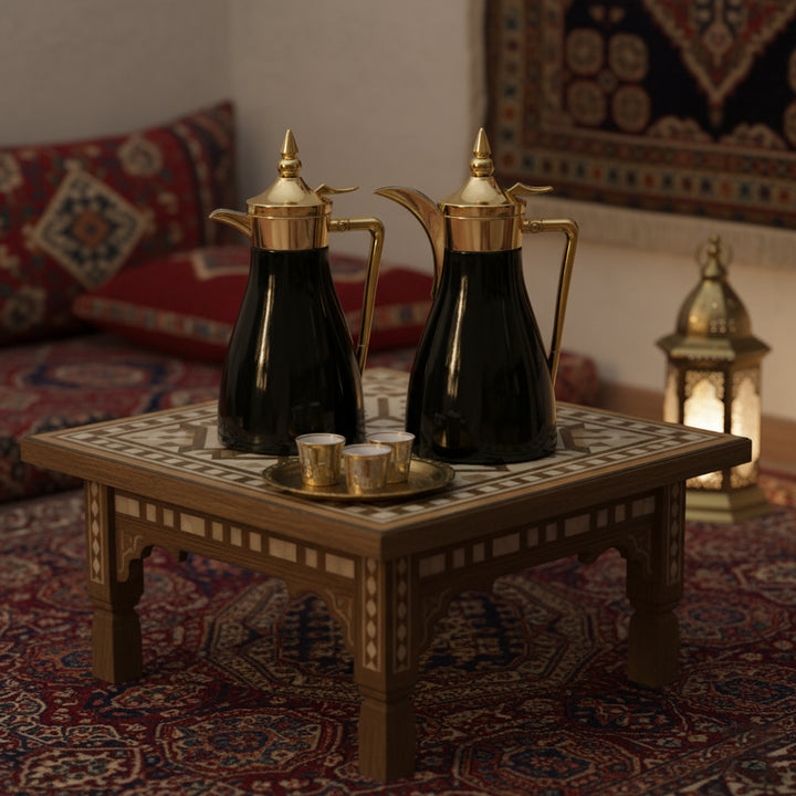 Two black and gold coffee pots on a small table with a decorative rug and lantern in the background.