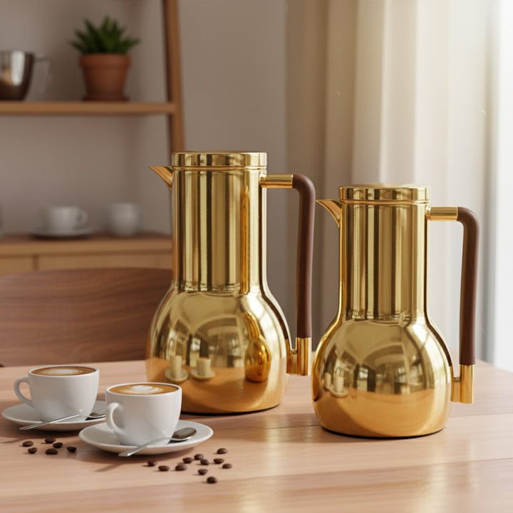 Two gold coffee pots on a wooden table with coffee cups and beans.