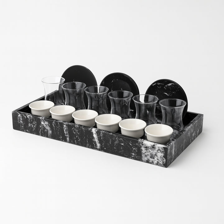 Set of ceramic cups and glasses on a black marble tray against a white background