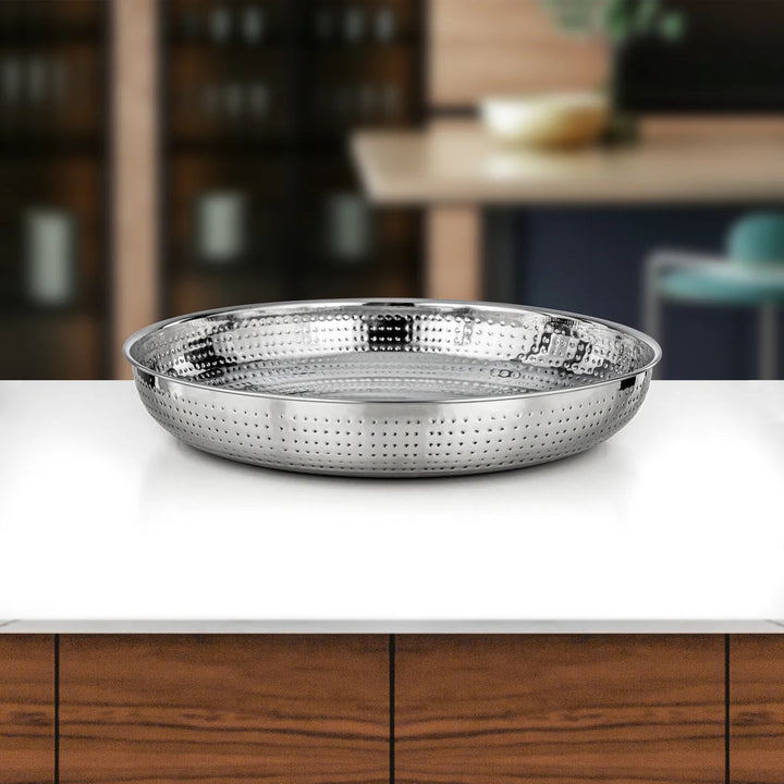 Silver perforated pan on a kitchen counter with blurred background