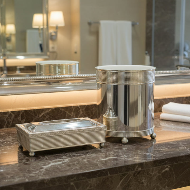Silver bathroom accessories on a marble countertop with a mirror and towels in the background.