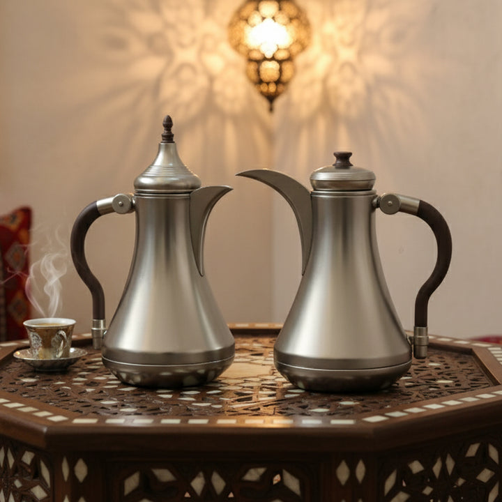 Two silver coffee pots on a decorative table with a warm background