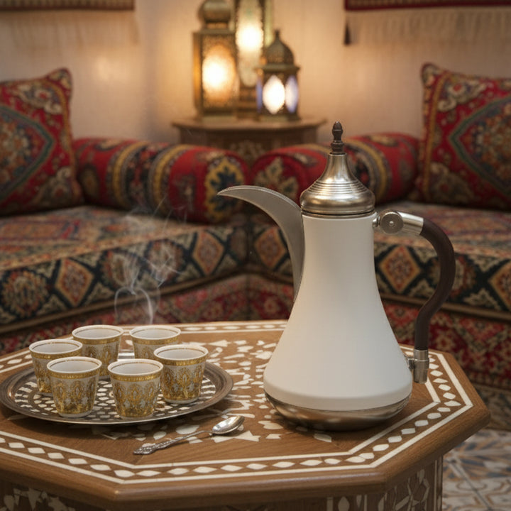 Traditional white coffee pot with silver accents on a decorative table in a cozy room with patterned sofa and lanterns.