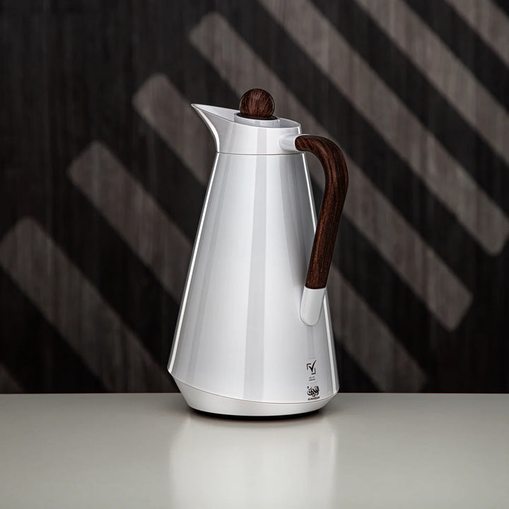 Silver coffee pot with wooden handle and lid on a reflective surface with a dark, striped background