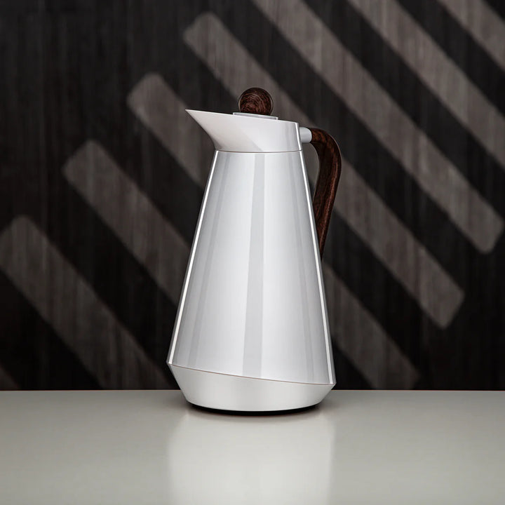 Silver coffee pot with a wooden handle on a reflective surface with a dark, striped background