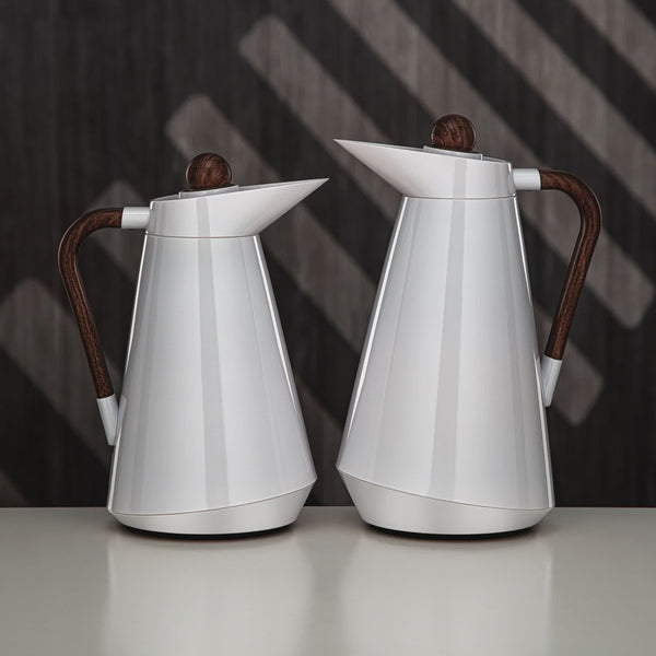 Two silver coffee pots with wooden handles on a reflective surface and dark background