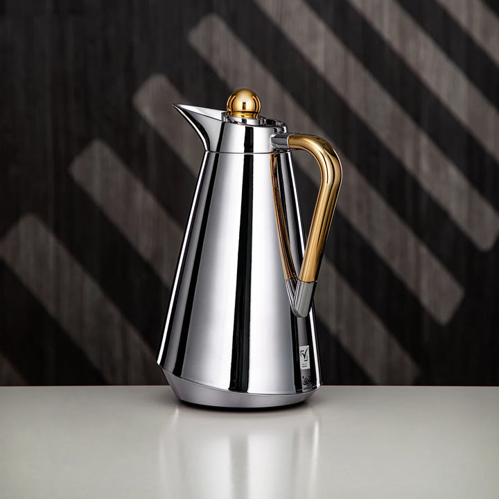 Stainless steel coffee carafe with gold accents on a dark background