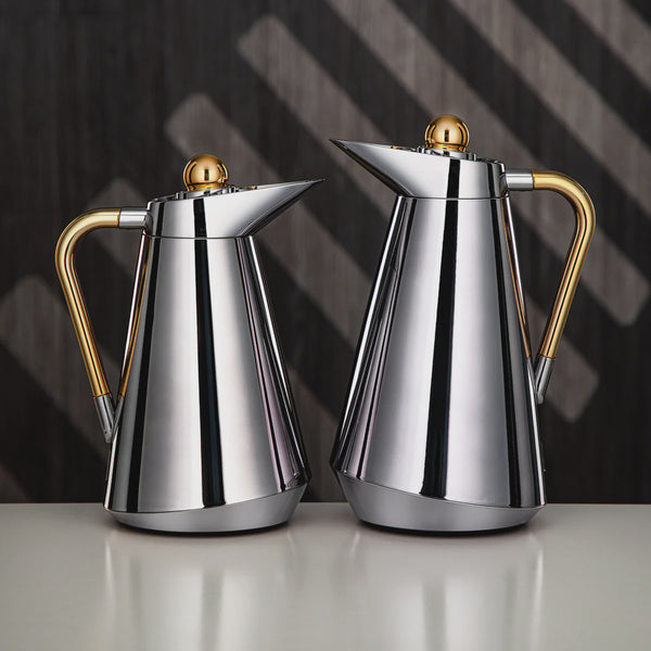 Two silver and gold coffee pots on a reflective surface with a dark background
