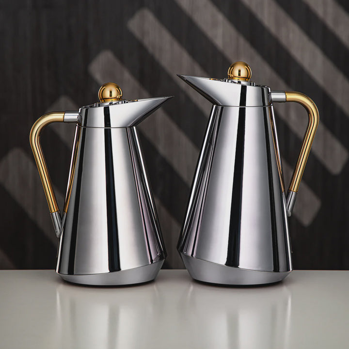 Two silver and gold coffee pots on a reflective surface with a dark background