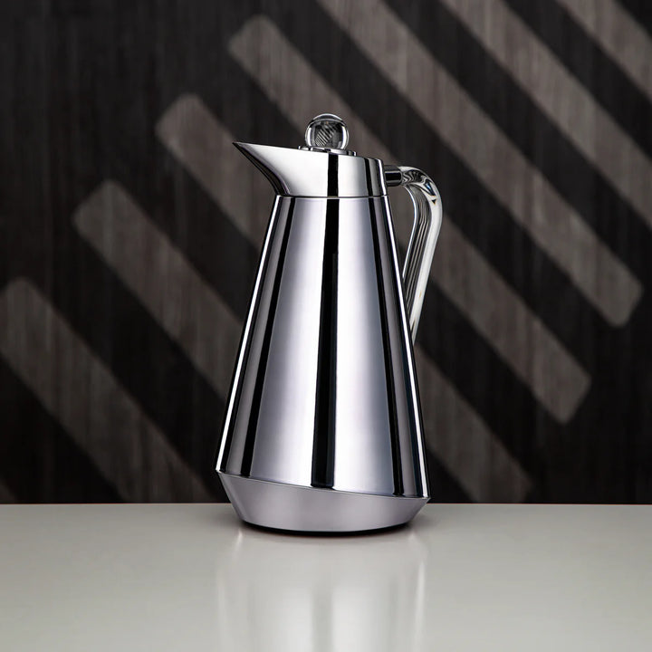Silver coffee pot on a reflective surface with a dark, striped background