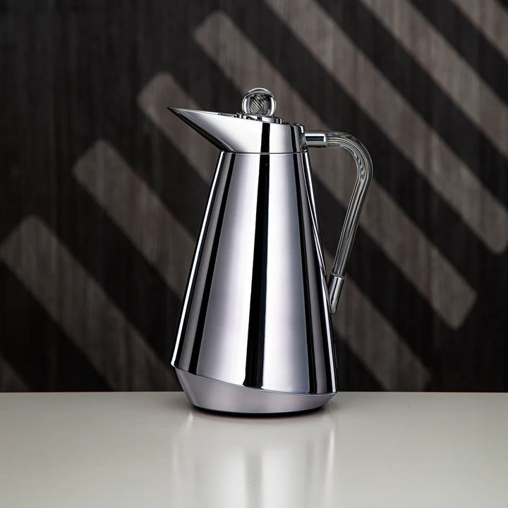 Stainless steel coffee pot on a reflective surface with a dark, striped background