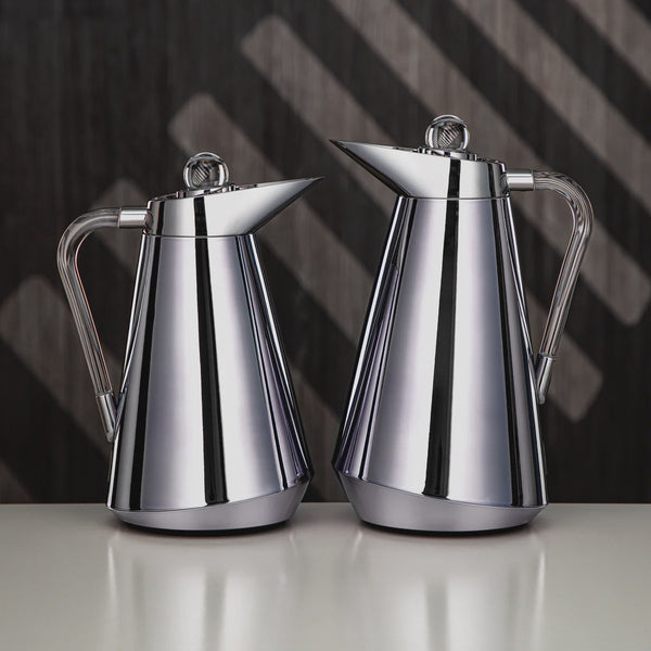 Two silver coffee pots on a reflective surface with a dark geometric background