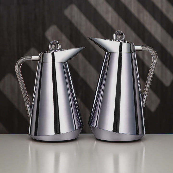 Two silver coffee pots on a reflective surface with a dark geometric background