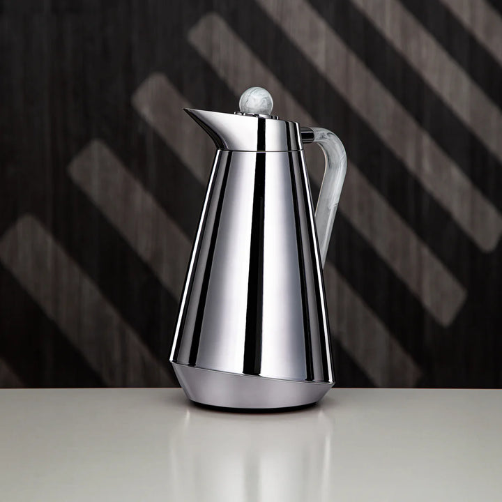 Silver coffee pot on a reflective surface with a dark, striped background