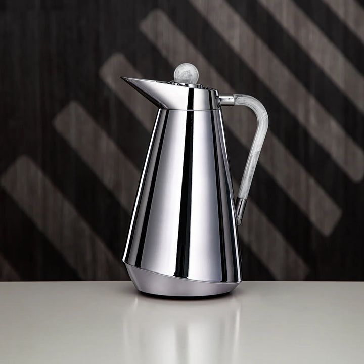 Silver coffee pot on a reflective surface with a dark, striped background