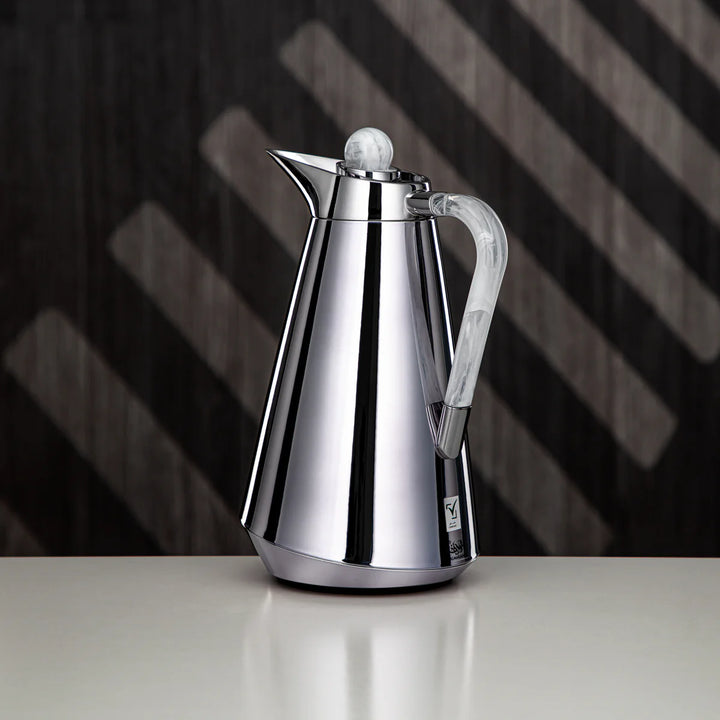 Stainless steel coffee pot on a reflective surface with a dark, patterned background