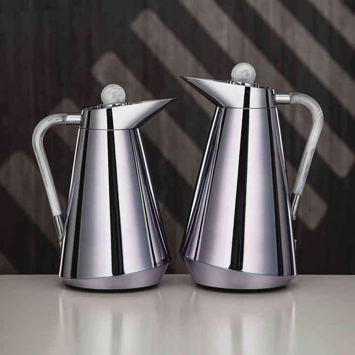 Two silver coffee pots on a reflective surface with a dark background