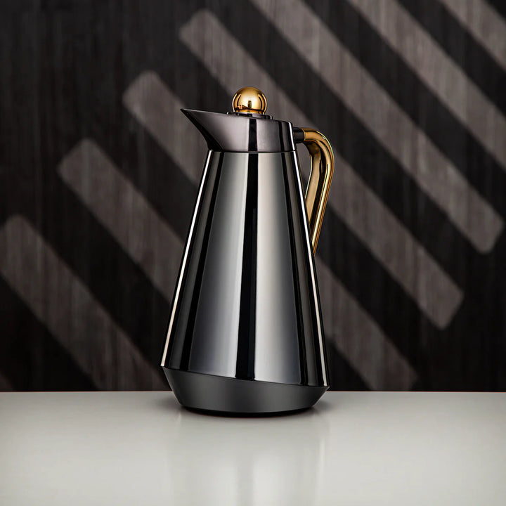 Stainless steel coffee carafe with gold accents on a dark background