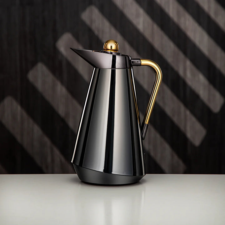 Stainless steel coffee pot with gold accents on a dark background