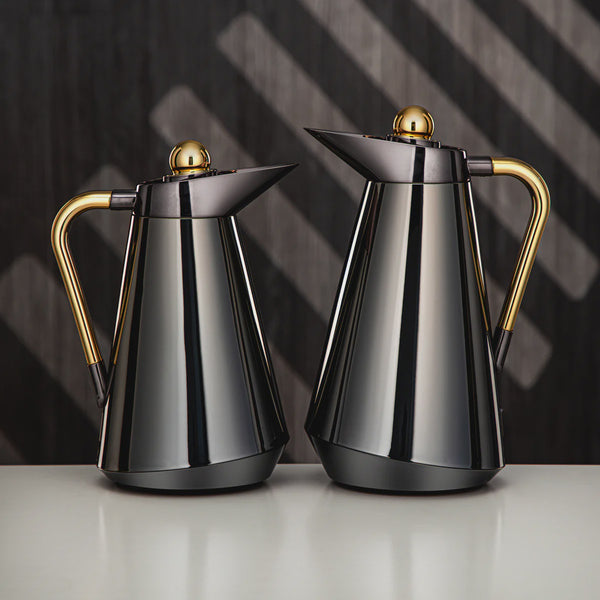 Two metallic coffee pots with gold handles on a reflective surface and dark background
