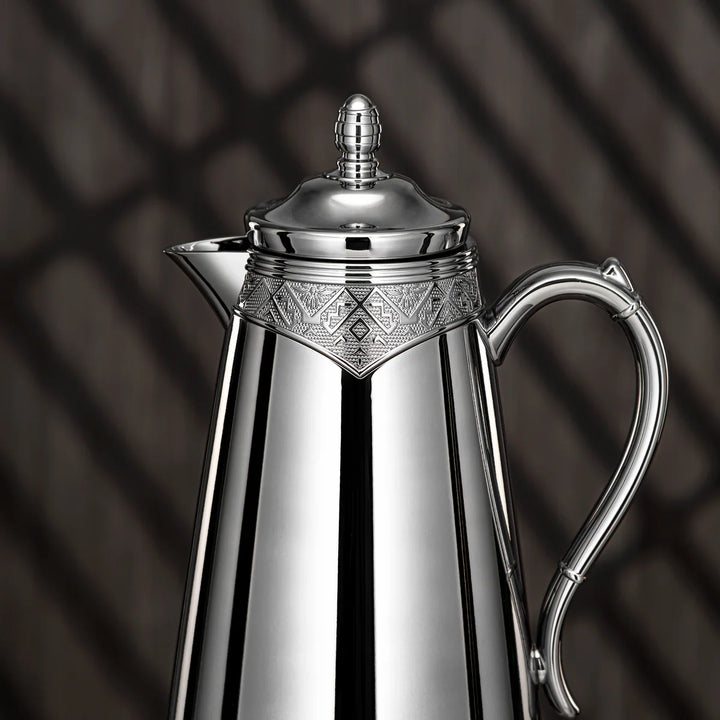 Silver coffee pot with intricate design on a dark background