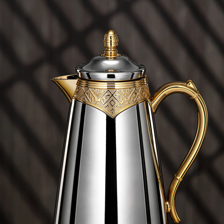 Silver and gold coffee pot with intricate design on a dark background