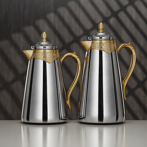 Two silver and gold coffee pots on a reflective surface with a dark background