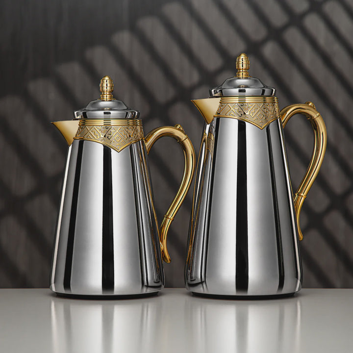 Two silver and gold coffee pots on a reflective surface with a dark background
