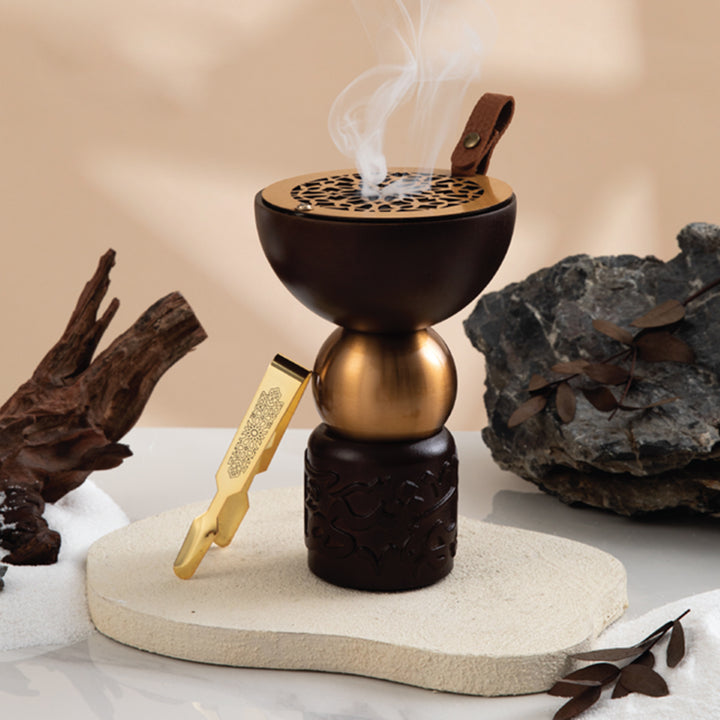 Decorative incense burner with smoke, gold tool, and natural elements on a neutral background