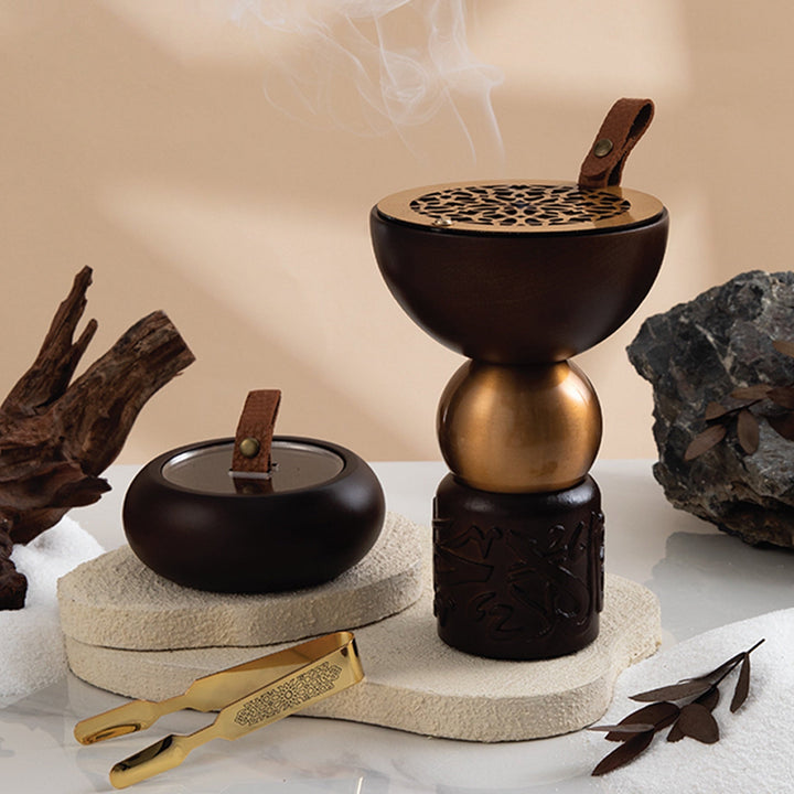 Decorative incense burner with smoke, rocks, and a gold tool on a neutral background