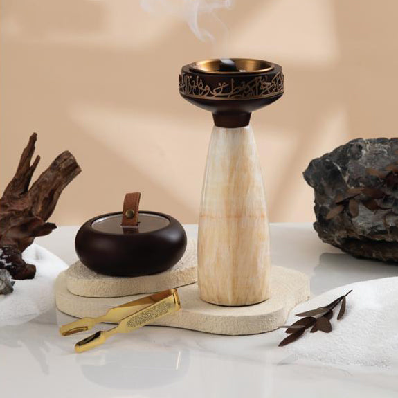 Decorative incense holder with smoking incense, rocks, and leaves on a neutral background