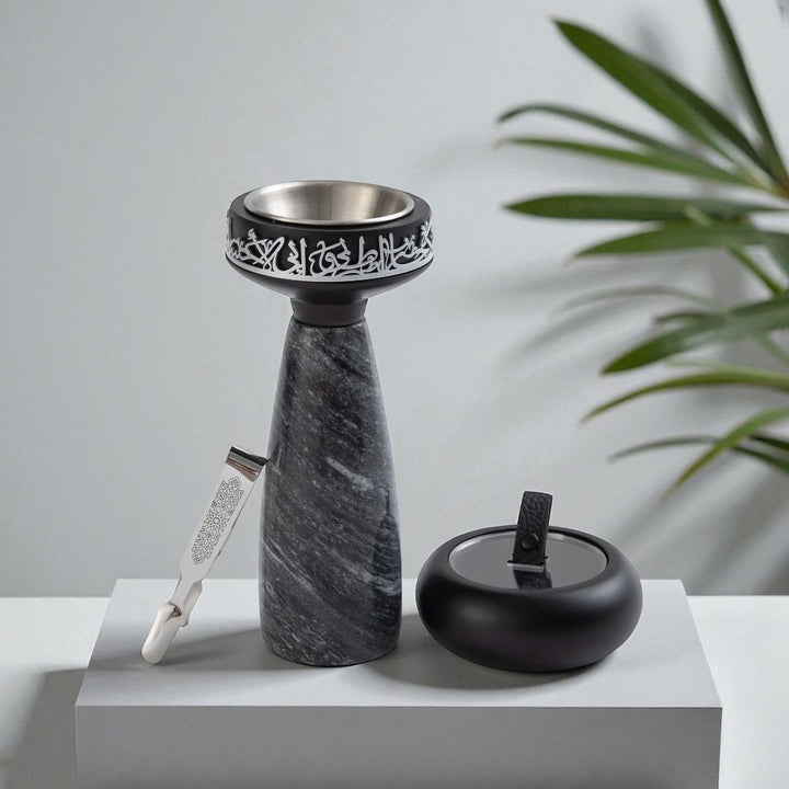 Decorative stone candle holder with intricate carvings on a white surface with a plant in the background.