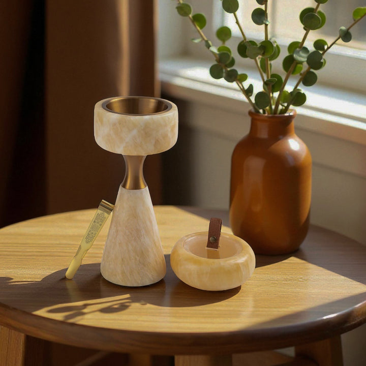 Decorative items including a candle holder, small bowl, and vase on a wooden table with a plant in the background.