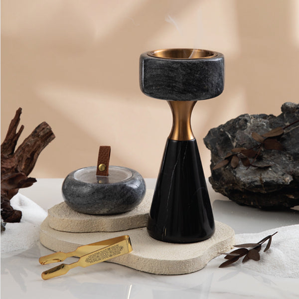 Decorative black and gold candle holder on a neutral background with rocks and tools.